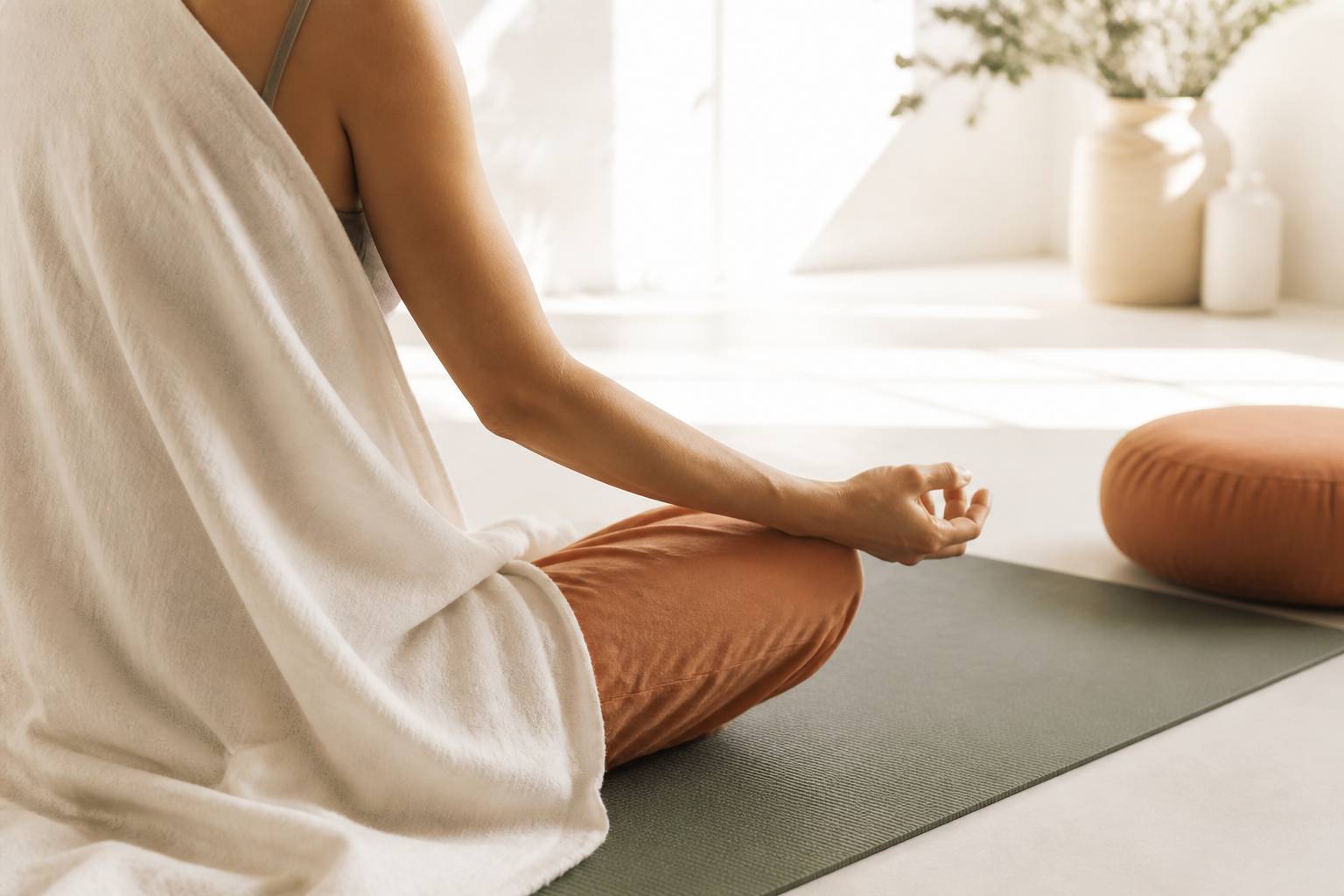 Personne vue de dos assise en tailleur sur un tapis de yoga